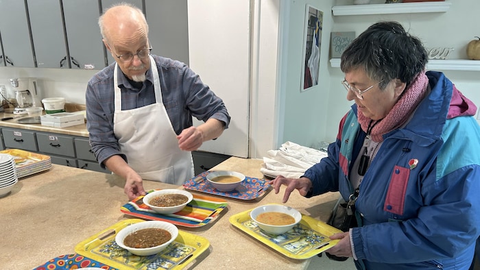 Un homme sert une soupe chaude à une femme dans un local communautaire.