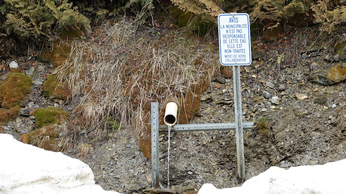Une pancarte à côté d'un tuyau qui laisse couler de l'eau.