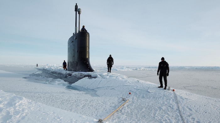 Des marin marchent sur la glace près de la tourelle d'un sous-marin qui émerge de la glace.