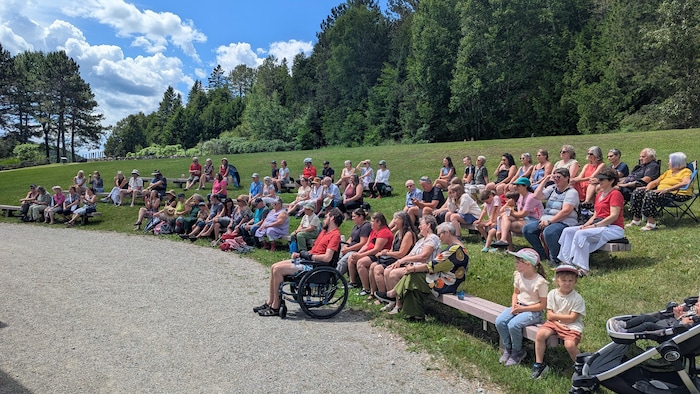 A little crowd sitting on benches look towards the stage.