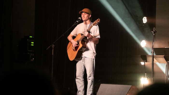 Un adolescent avec une guitare sur scène.