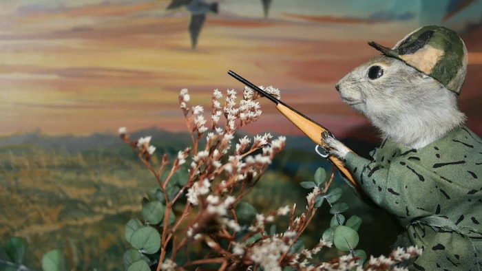 Une peinture sur toile montrant un rongeur habillé en humain et équipé pour la chasse.