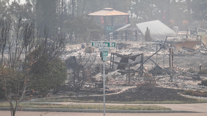 Un panneau d'intersection partiellement fondu devant les ruines d'un bâtiment emporté par les flammes.