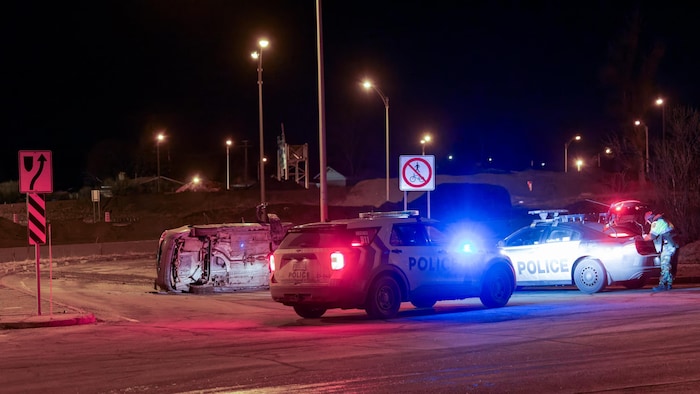 A wrecked car in front of police cars.