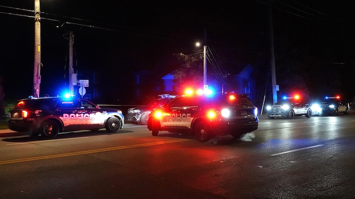Des véhicules de police devant un périmètre de sécurité.