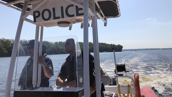 Deux policiers regardent au loin alors qu'ils naviguent sur un plan d'eau.