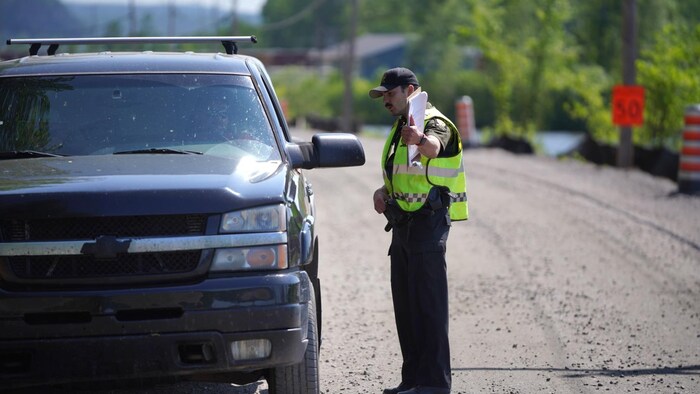 Un officier de la Sûreté du Québec discute avec le conducteur d'une camionnette et semble lui donner des indications.