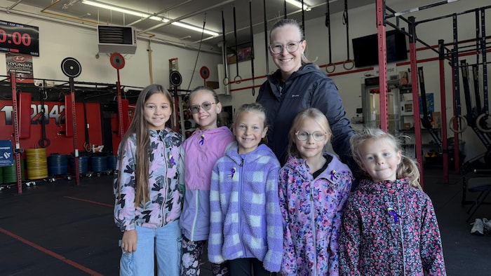 Une femme adulte et cinq fillettes souriantes posent ensemble à l'intérieur d'une salle d'entraînement.