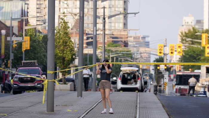 Une jeune fille soulève un ruban policier pour passer dessous sur l’avenue St. Clair Ouest à Toronto le 12 juillet 2026.