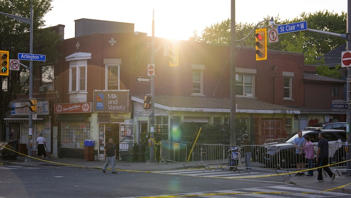 Des piétons marchent sur l’avenue St. Clair Ouest à Toronto le 12 juillet 2026. On peut voir un véhicule policier et des rubans jaunes.