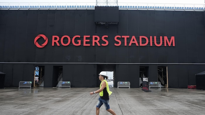 Un employé portant une veste de sécurité marche devant l'entrée du stade.