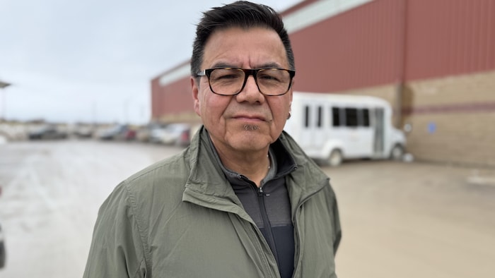 Un homme avec un imperméable regarde à la caméra,