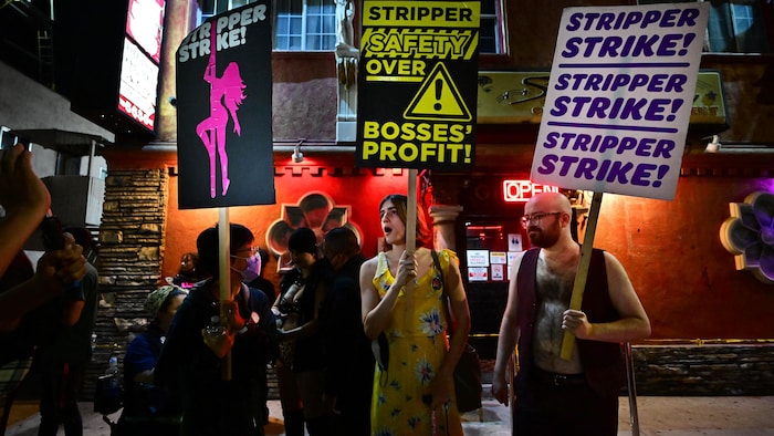 Des manifestants, pancartes à la main, devant un bar.