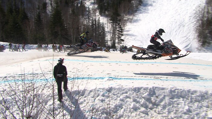 Deux motoneigistes effectuent un saut sur un parcours en neige.