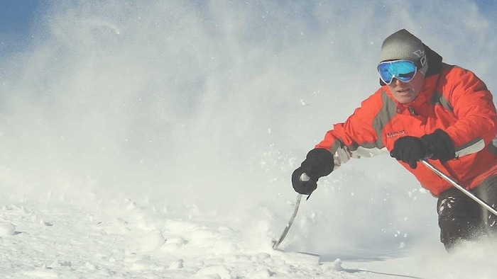 Un homme en vêtement orange fait du ski.