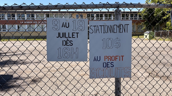 Deux affiches accrochées à un grillage devant un stationnement.