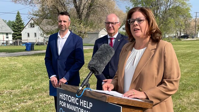 La première ministre du Manitoba, Heather Stefanson, prononce un discours devant un podium à l’extérieur au mois de juin. Derrière elle, deux hommes en complets.
