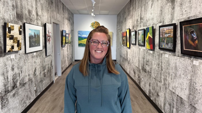Stéfanie Thompson est entourée d'œuvres sur les murs d'une galerie d'art.