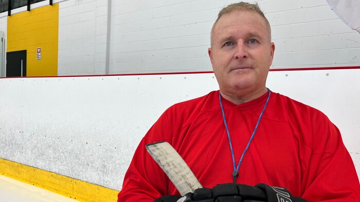 Stéphane Asselin pose à la caméra avec un bâton de hockey dans les mains.