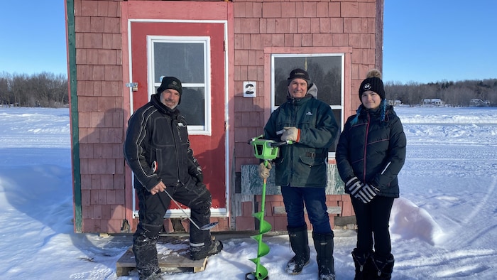 Mathieu Côté, Stéphane Girouard et la fille de Stéphane, Charlie, posent devant une cabane de pêche.