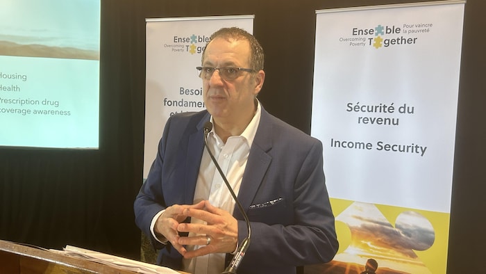 Un homme parle dans un micro, des bannières derrière lui.