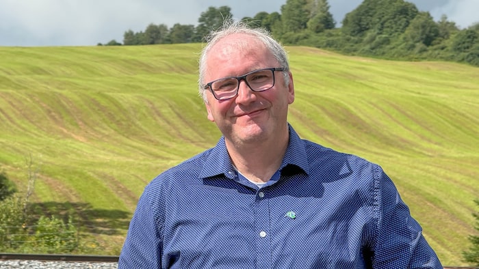 Portrait de Stéphane Pineault, un champ agricole en arrière-plan.