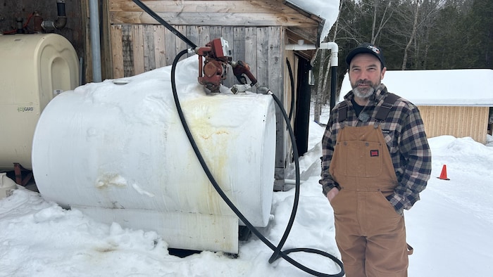 Stéphane Roy, le propriétaire Érablière des Écorchis, est en salopette à côté d'une cuve de pétrole.
