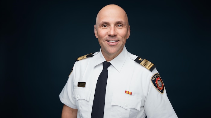 Stéphane Sigouin, portant cravate et chemise de pompier, sourit pour la caméra sur une photo officielle.