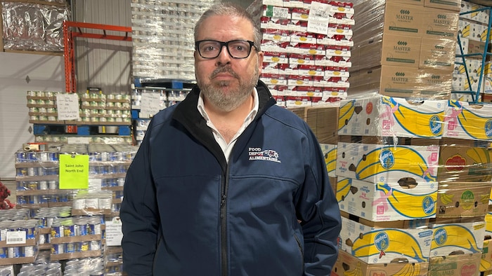 Un  homme regarde la caméra, des boîtes et conserves derrière lui.