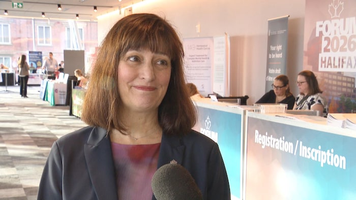 Stéphanie Bélanger accorde une entrevue dans un centre de conférence, à gauche d'un kiosque identifié comme celui de l'inscription.