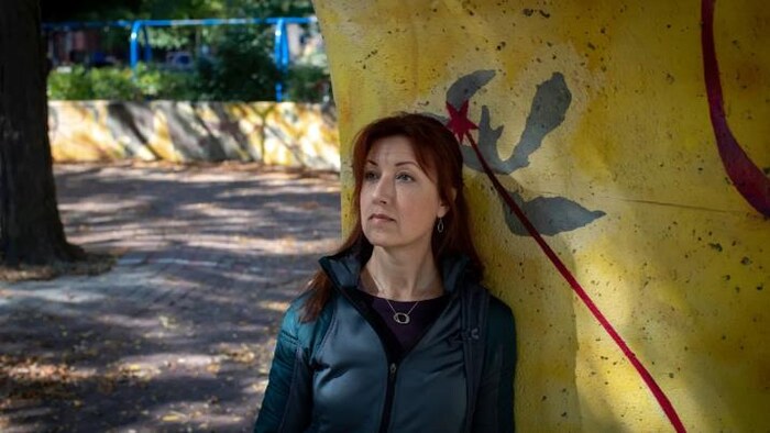Une femme est adossée à un mur, dehors.