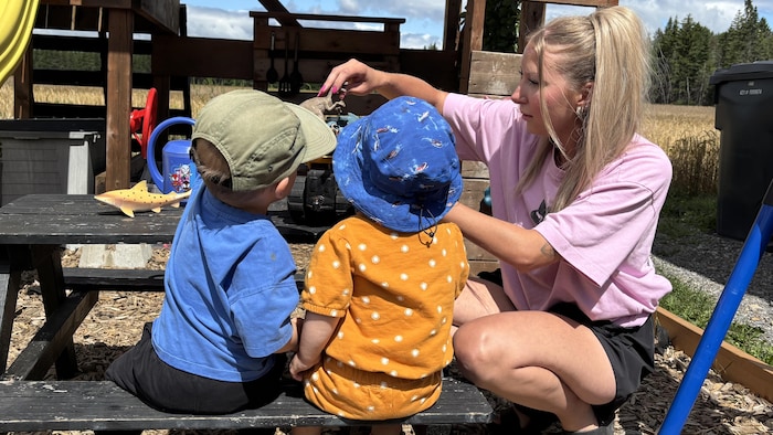 Une femme joue avec deux enfants dans modules de jeux.