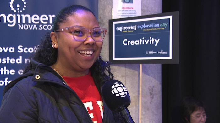 Une femme accorde une entrevue à côté d'une affiche bleue avec le mot «créativité» imprimé.