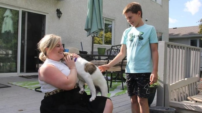 Stephanie Laubenstein accroupie a dans ses bras son chien et son fils Benjamin est debout près d’elle.