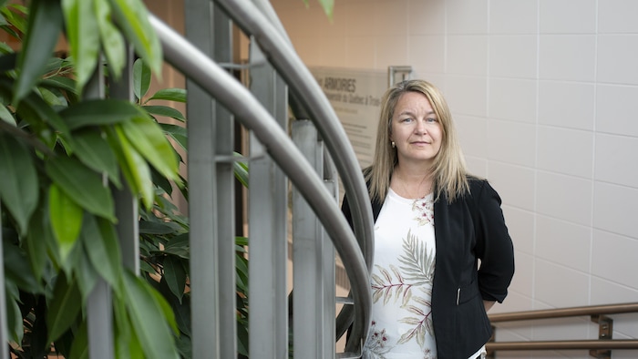 Une femme prend la pose dans un escalier avec des feuilles d'une plante en avant-plan.