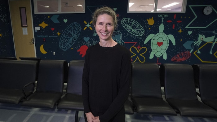 Stéphanie Marsan debout dans une salle d'attente décorée d'une murale.