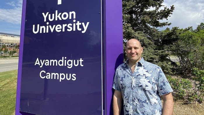 Un portrait de Stephen Biggin-Pound près d'une enseigne de l'Université du Yukon.