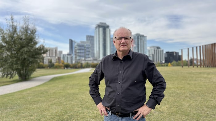 Un homme avec une chemise met les mains sur ses hanches, avec la ville de Calgary en arrière-plan.