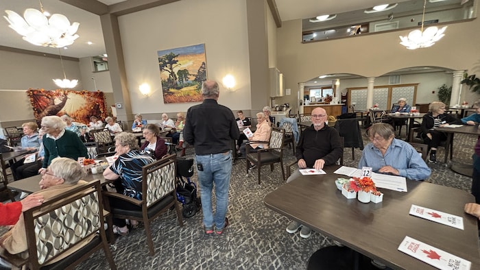 Un homme parle à des retraités dans une salle à manger.
