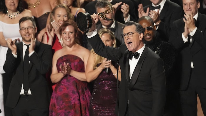 Stephen Colbert, au centre, entouré de lad   équipe avec un trophée dans les mains.