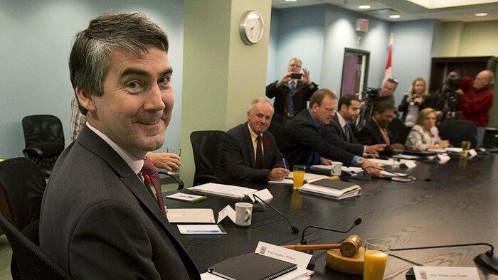 Stephen McNeil, assis à une grande table avec les membres de son cabinet, se tourne vers le photographe et sourit.