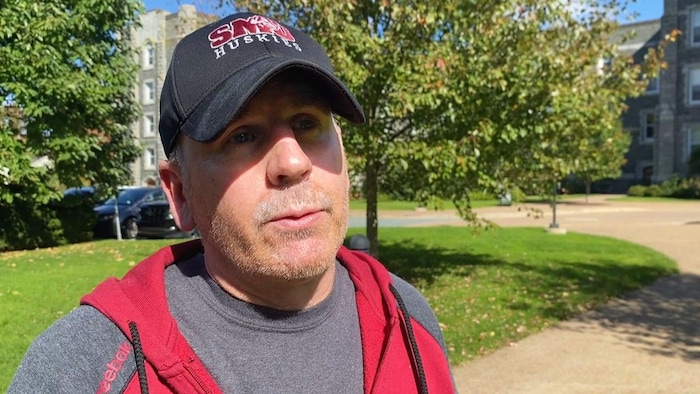 Un homme portant une casquette de baseball des Huskies de Saint Mary's est dehors dans un parc, en été.