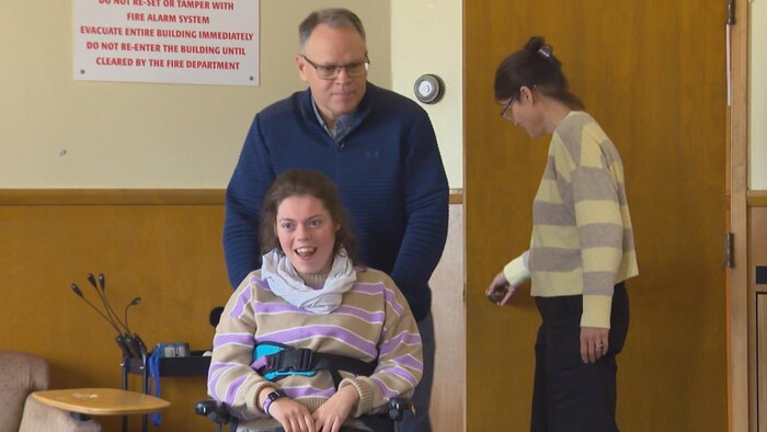 Un homme pousse le fauteuil roulant d'une jeune adulte.