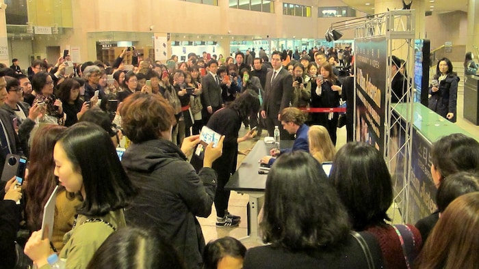 Steve Barakatt assis à une table signe des autographes devant une foule.