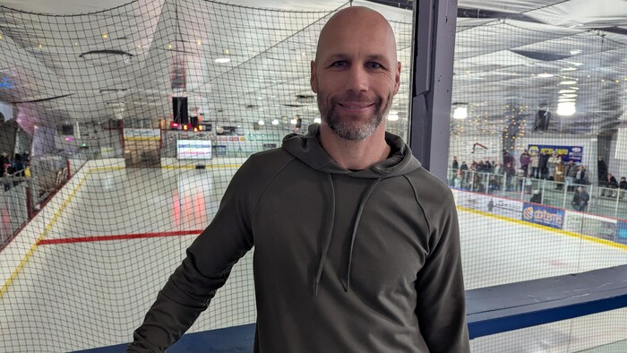 Steve Bégin sourit à la caméra en posant devant une patinoire.