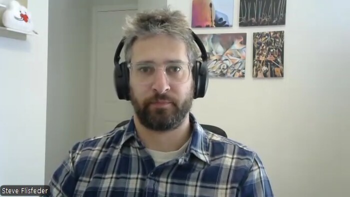 Portrait de Steven Flisfeder en entrevue qui porte une chemise à carreaux, des lunettes et un casque d'écoute.