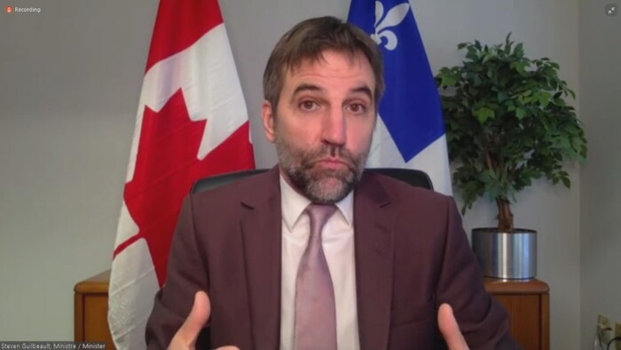 Assis à son bureau, un homme répond aux questions des journalistes lors d'une conférence virtuelle.