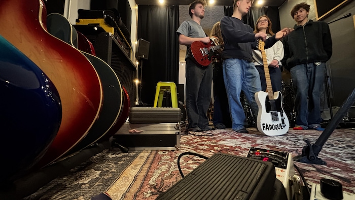 En avant-plan des guitares, derrière, les cinq membres du groupe en entrevue pour le reportage.