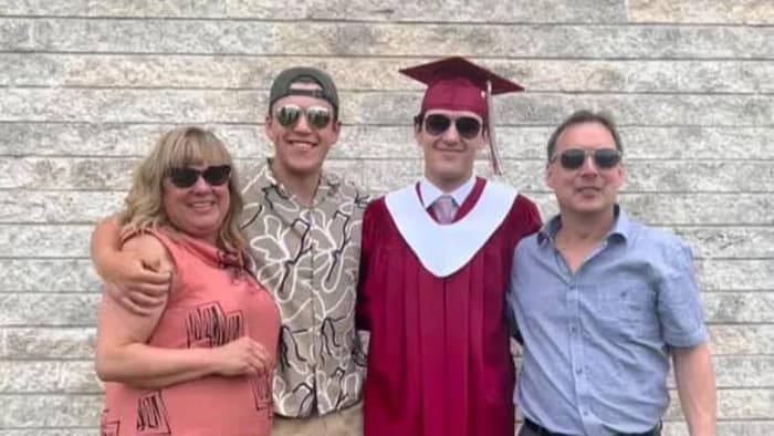 Une femme, un jeune homme, un autre jeune homme en tenu de remise de diplôme et un homme plus âgé.