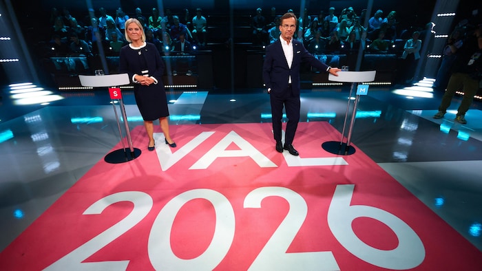 Une femme et un homme se tiennent côte à côte dans un studio de télé.